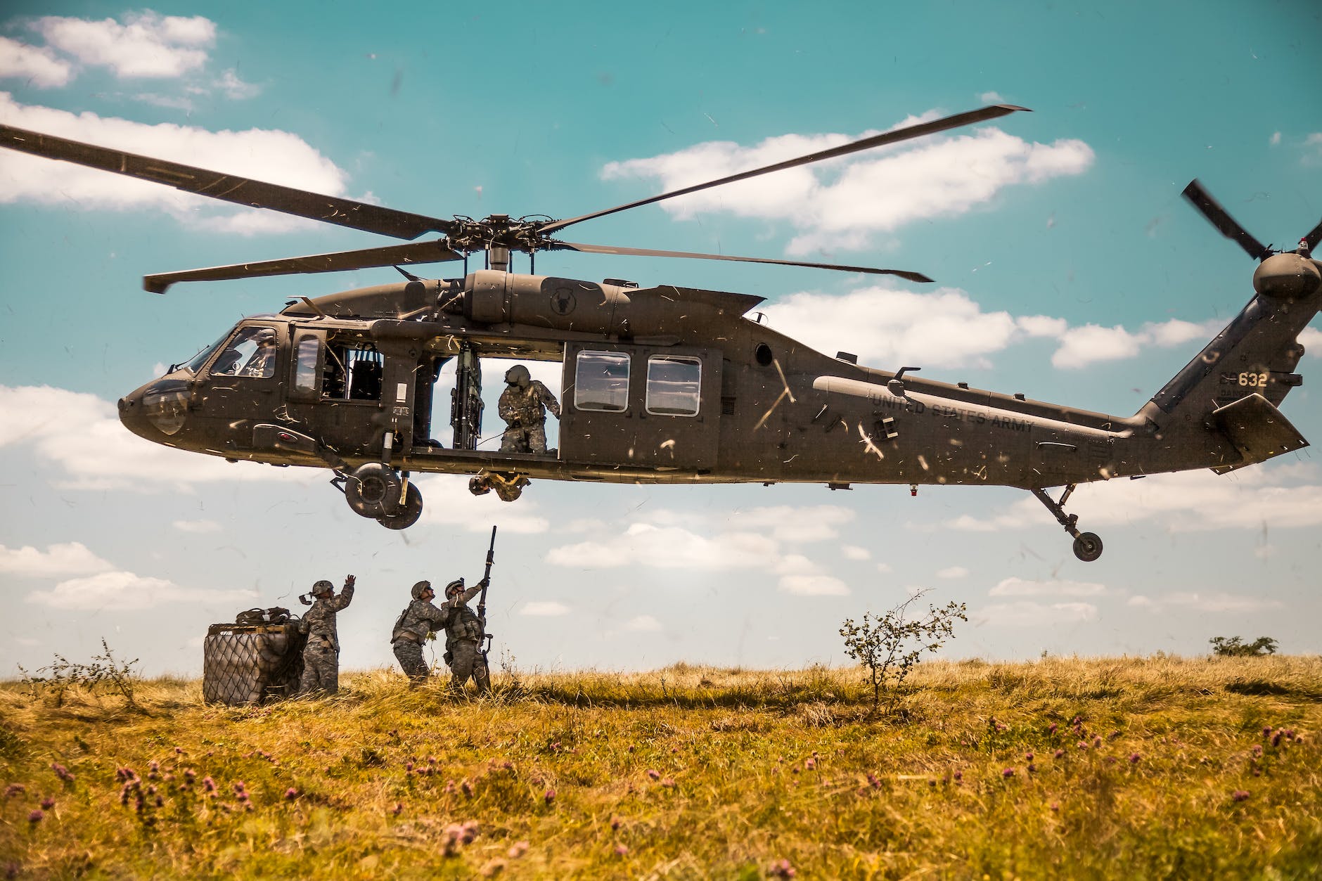 a us army helicopter hovering above a group of soldiers