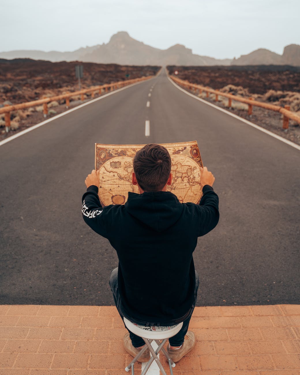 man in black hoodie holding a map in the middle of the road