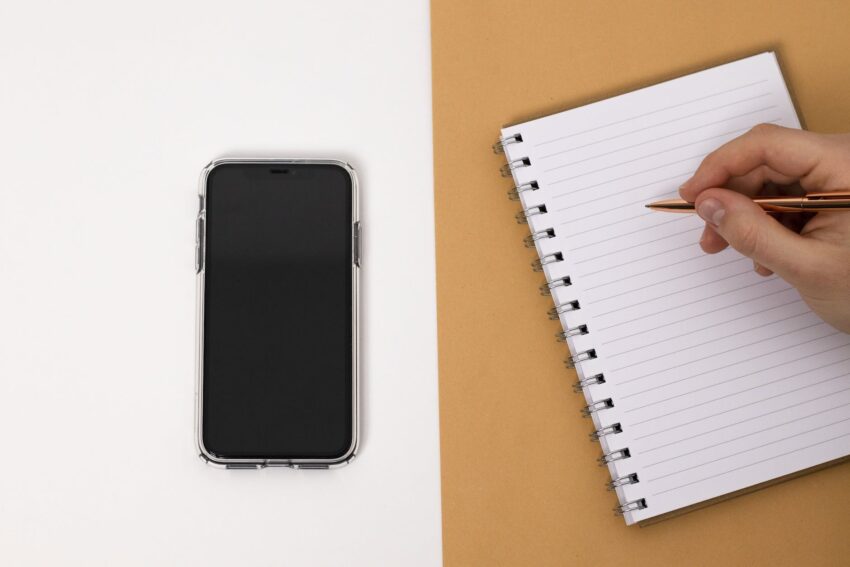 a cell phone and a person writing in a notebook