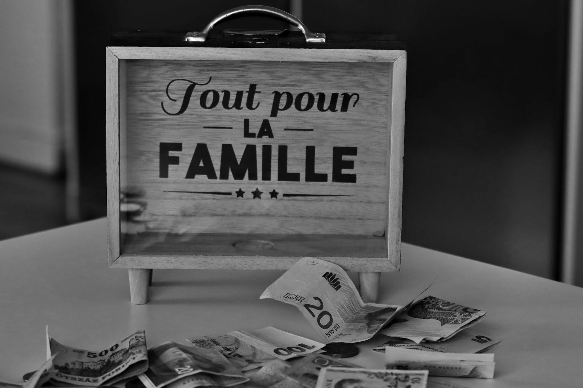 French: Tout pour La Famille English translation: Everything for the family a wooden case beside a bunch of paper money on white table